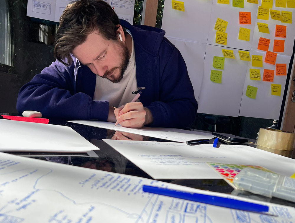 Séance de travail devant un mur de post-its, croquis d'interface en cours
